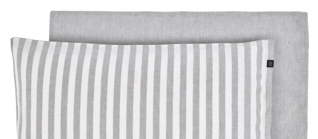 A neatly folded bedding set consisting of a pillowcase—the stripes show vertical gray and white stripes—and a matching plain light gray sheet, both made of a linen-like fabric.