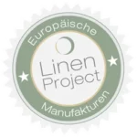 A circular green and white badge with the text European Linen Project Manufactories and a small crescent shape above the word Linen. White stars are located on both sides of Project.