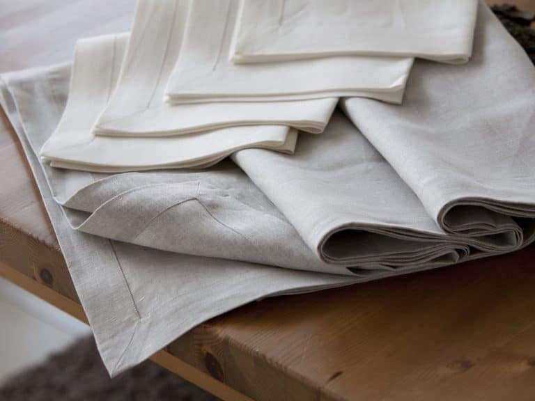 A pile of neatly folded beige and cream-colored linen napkins lies on a wooden table.