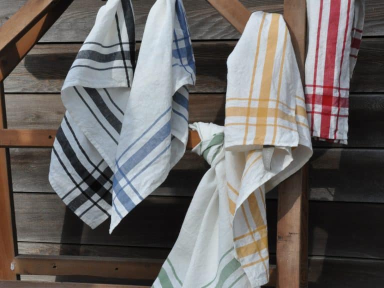 Das Camaret Black - reines Leinen für die Küche von Libeco und andere gestreifte Küchentücher in Schwarz, Blau, Gelb, Grün und Rot hängen in einem Holzrahmen an einer verwitterten Holzwand.