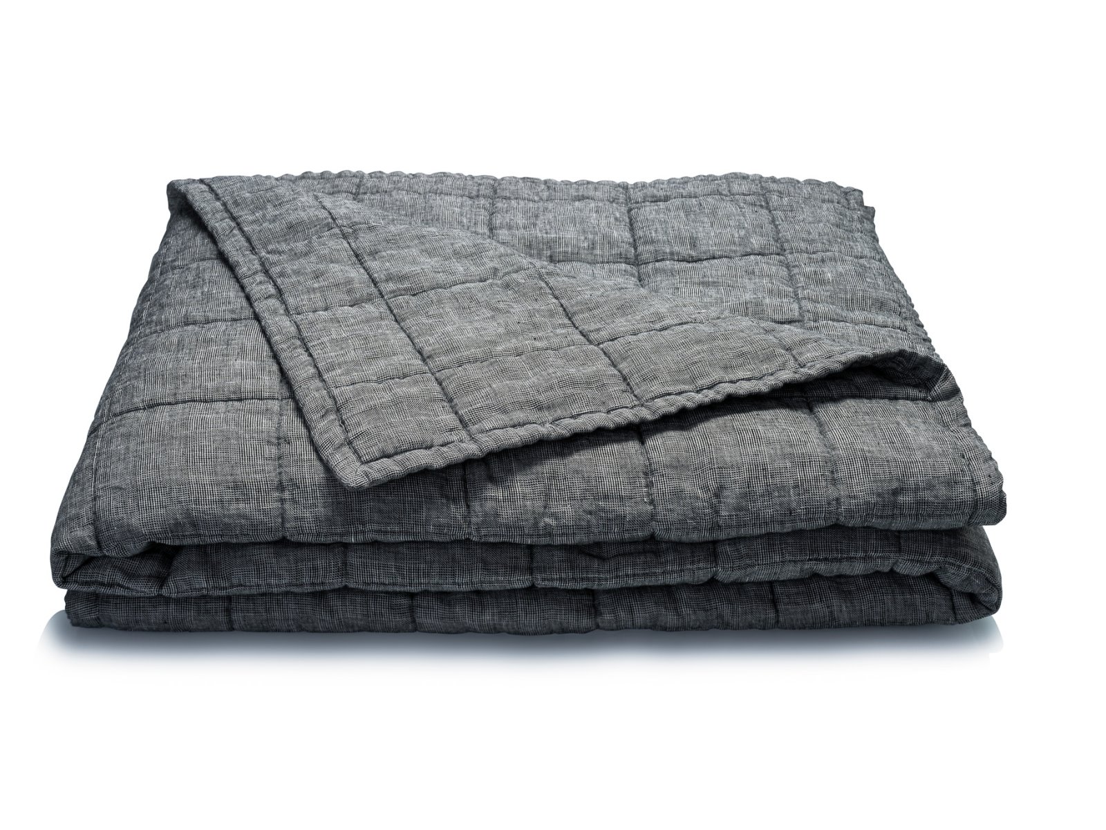 Die Scotia Leinen Tagesdecke von Geniksa, eine gefaltete graue Steppdecke mit einem strukturierten Muster, ist ordentlich auf einem weißen Hintergrund gestapelt, wobei eine Ecke umgeschlagen ist, um die Innenseite zu zeigen.