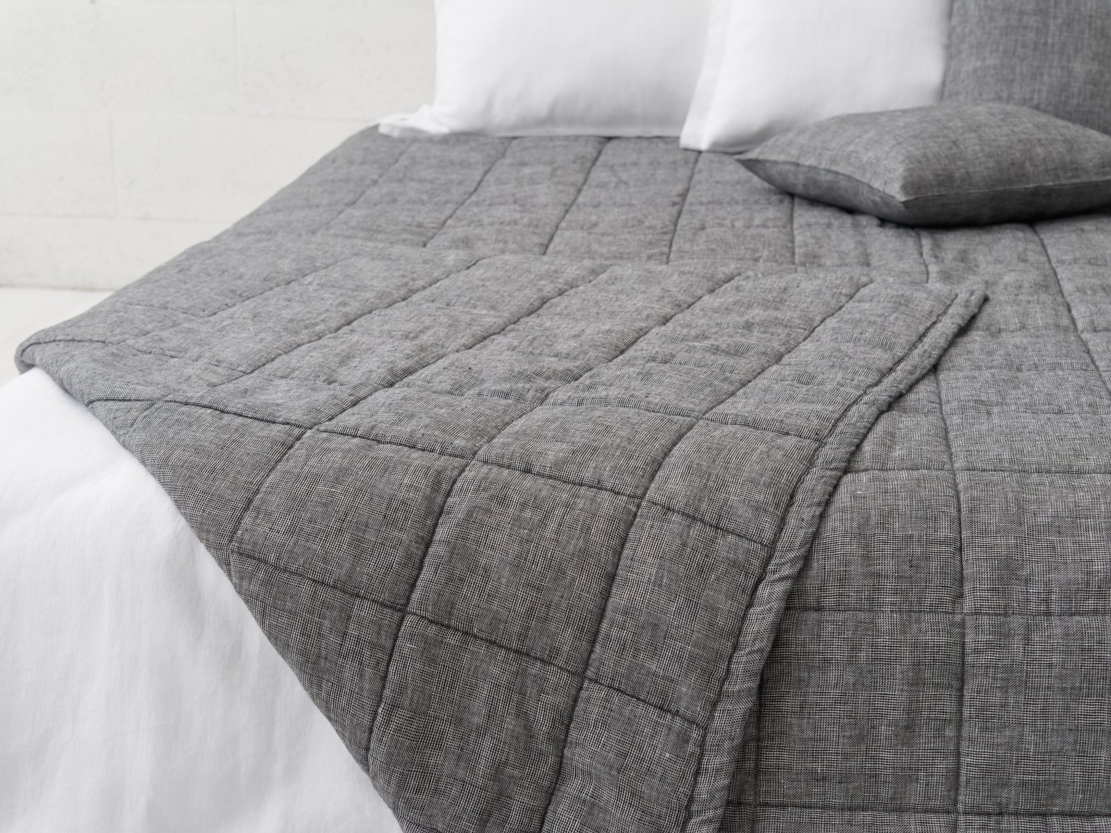 Eine Nahaufnahme eines ordentlich gemachten Bettes mit der Scotia Leinen Tagesdecke von Geniksa in Grau und zwei weißen Kissen. Der gitterartige, strukturierte Stoff der Decke verleiht dem Bettzeug einen modernen, gemütlichen Touch.