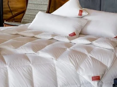 Ein ordentlich gemachtes Bett mit der KlimaControl Comfort Winterdecke von HEFEL - weißes, gestepptes Bettzeug mit zwei großen weißen Kissen, die jeweils mit einem roten Etikett versehen sind. Ein dunkles Kopfteil, ein Sessel und eine Holzvertäfelung sorgen für einen eleganten Hintergrund.