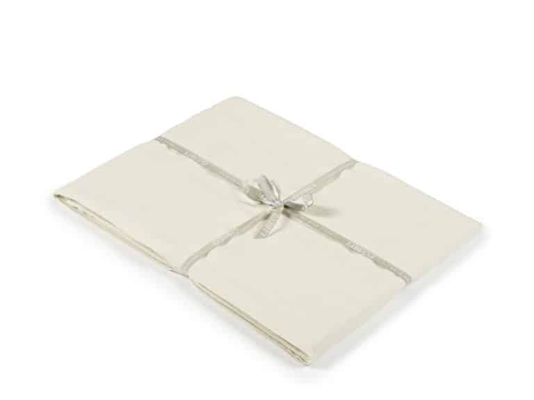 A neatly folded cream-colored fabric cloth tied together with a light gray ribbon with white print on a white background.