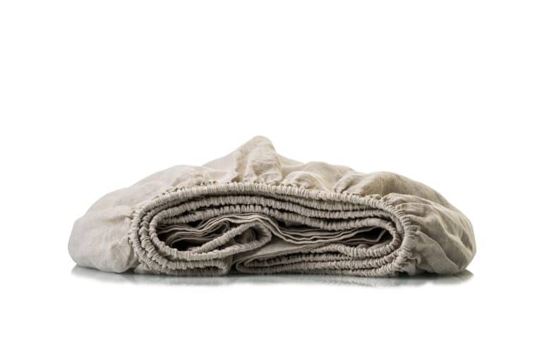 Ein ordentlich gefaltetes beiges Spannbettlaken mit elastischen Rändern, das Bettlaken aus starkem Naturleinen von Hoffmann, ist auf weißem Hintergrund abgebildet.