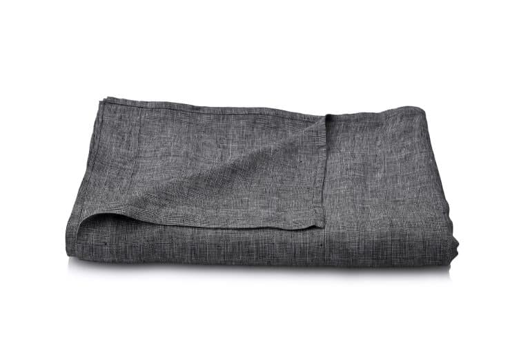 A neatly folded dark grey linen fabric on a white surface, with one corner slightly raised to reveal the texture and weave of the fabric.