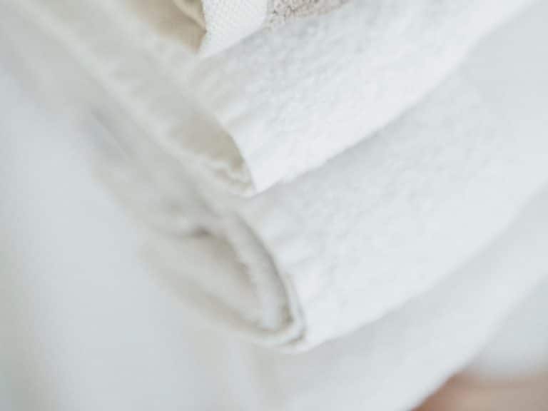 Eine Nahaufnahme von ordentlich gefalteten weißen Handtüchern, die übereinander gestapelt sind und deren weiches, strukturiertes Gewebe zur Geltung kommt.