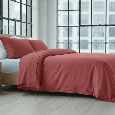Ein modernes Schlafzimmer mit großen Gitterfenstern, einem Holzbettgestell, Hanf und Leinen Bettwäsche Burgunder von Vieböck 226/30, einem hellen Holznachttisch und einer weißen Vase mit dekorativen Blättern auf einem hellen Holzboden.