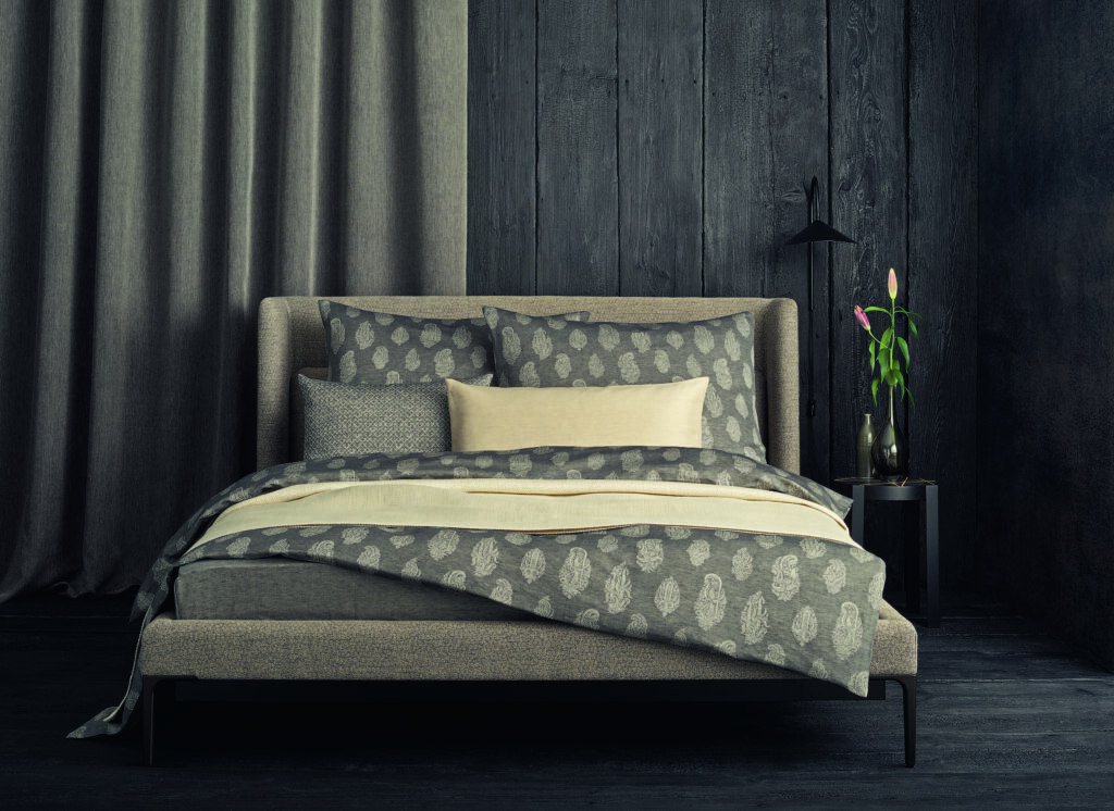 Ein Bett mit einer grau-weißen Bettdecke und Kopfkissen.