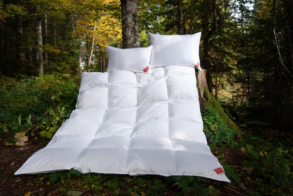 A white bed in the middle of a forest.