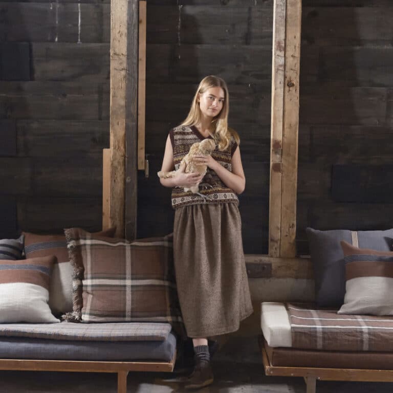 A woman stands next to a couch with cushions on it.