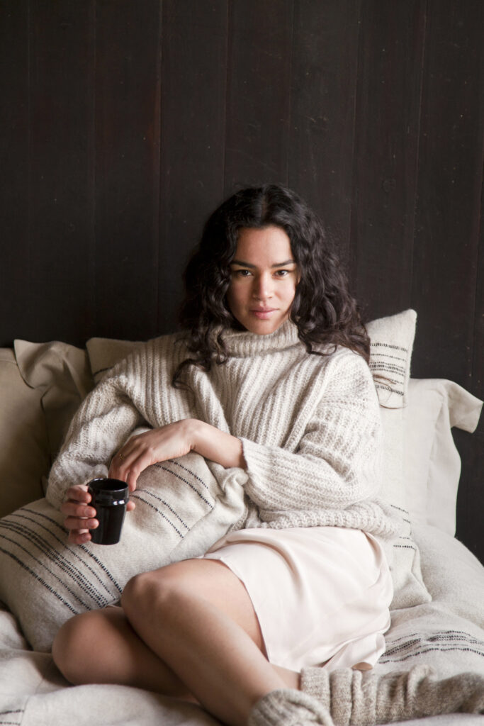 Eine Frau, die auf einem Bett sitzt und eine Tasse Kaffee in der Hand hält.