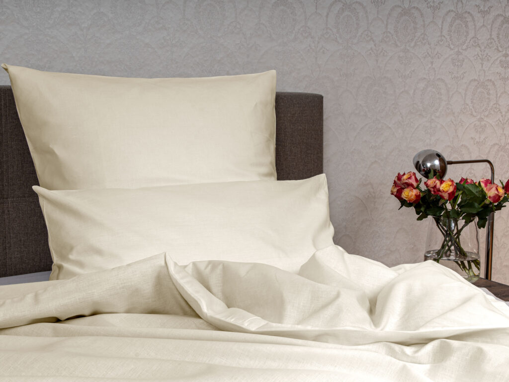 Ein Bett mit weißen Laken und einer Vase mit Blumen.