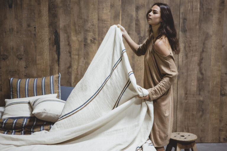 Eine Frau hält eine Decke über ein Bett.