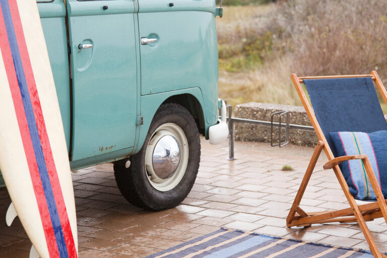 A blue VW bus parked next to a beach chair.