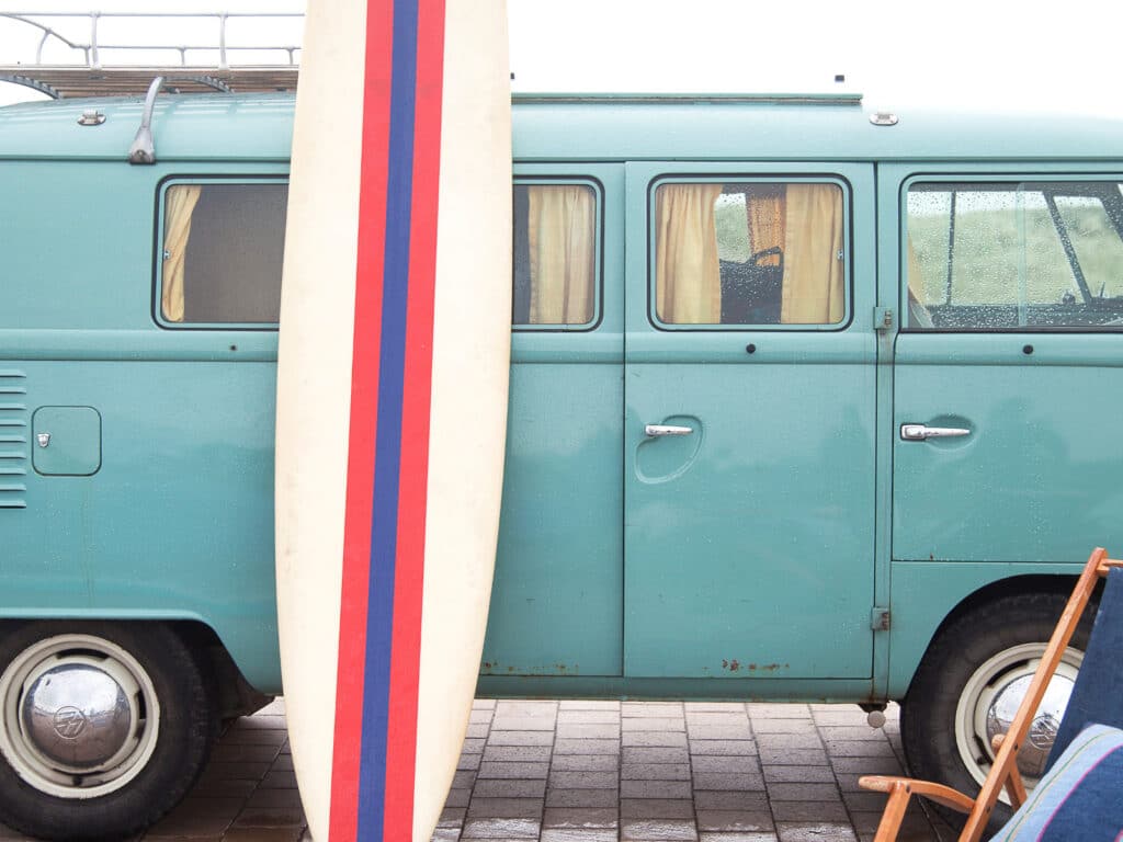Ein blauer Lieferwagen parkt neben einem weißen Surfbrett.