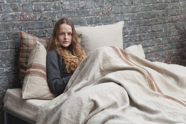A woman sitting on a bed with a blanket over her.