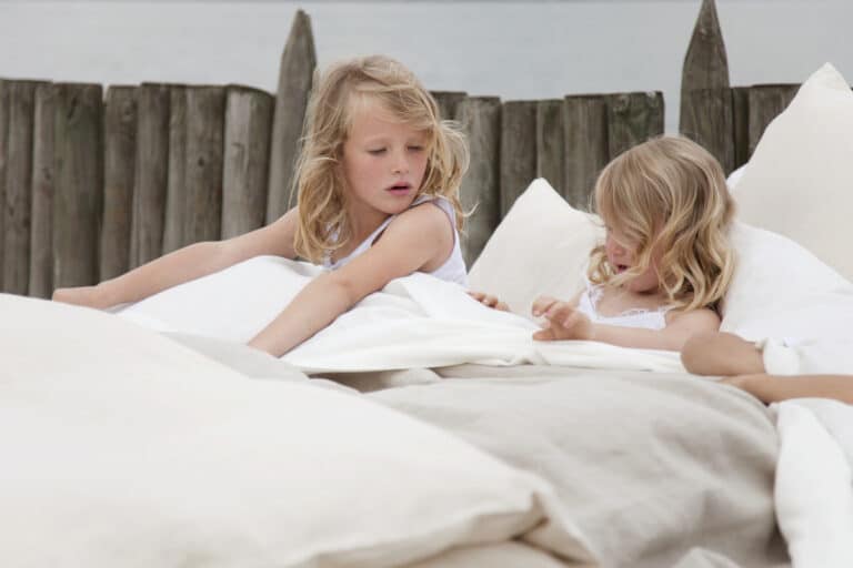 Zwei kleine Mädchen liegen in einem Bett mit weißen Laken.