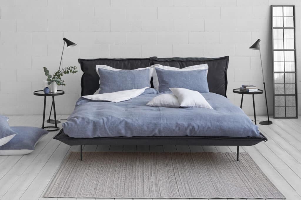 Ein Bett mit blauen Laken und Kissen in einem weißen Zimmer.