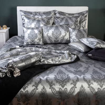 A bed with a silver and black duvet and pillows.