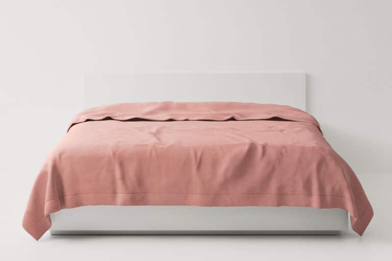 Ein Bett mit rosa Bettdecke und weißem Kopfteil.