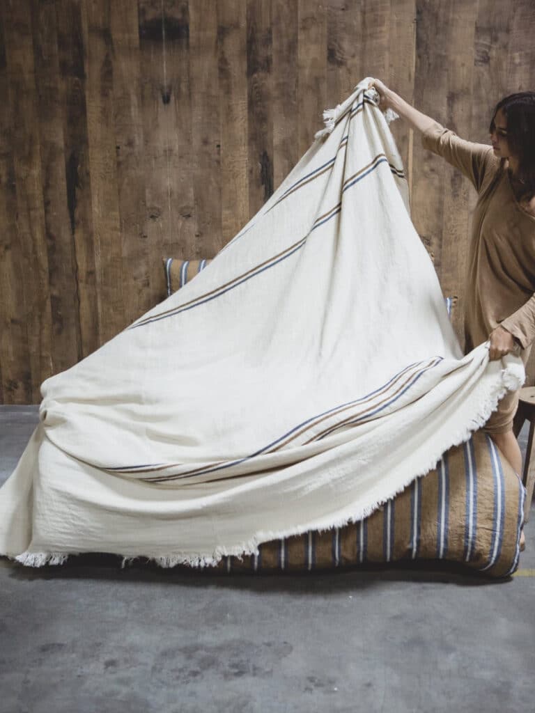 A woman is putting a blanket over a bed.