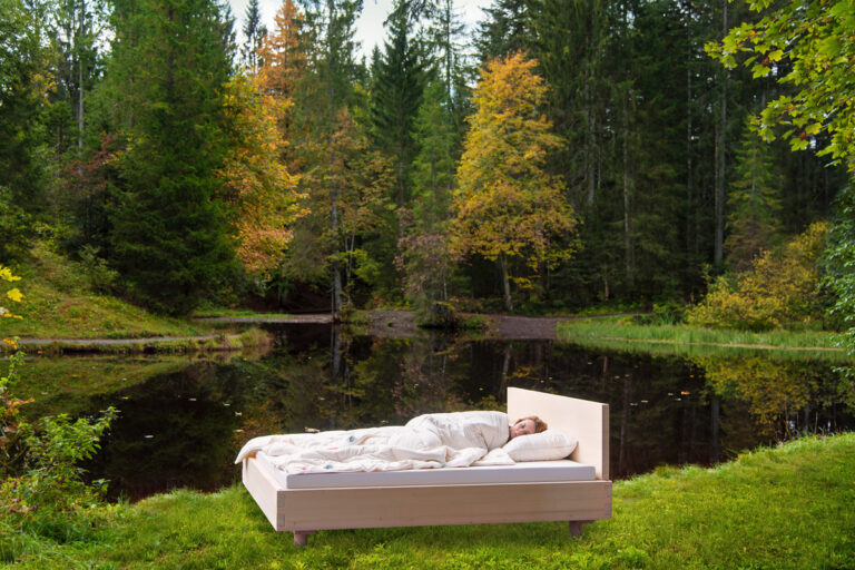 A person lying on a bed in the middle of a forest.