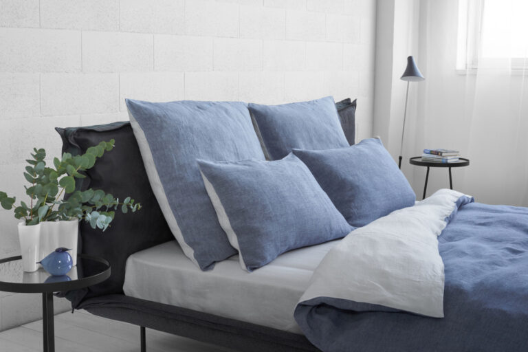 A bed with blue and white sheets and pillows.