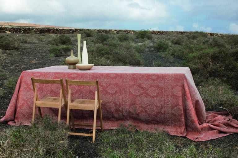 Einen Tisch mit einem roten Tischtuch und zwei Stühlen.