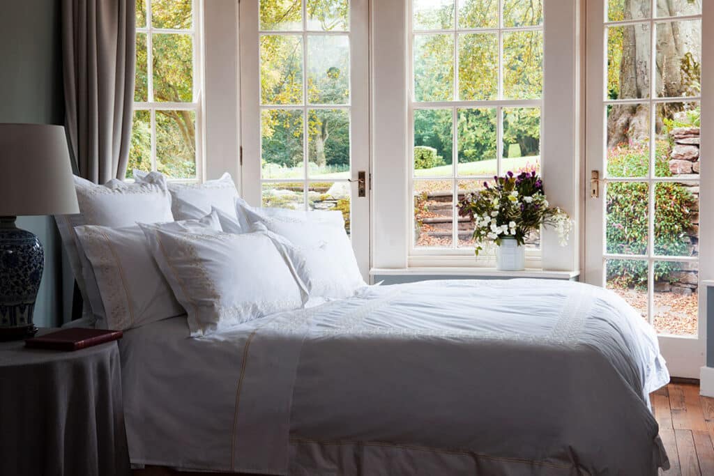 Ein Bett mit weißen Laken und Kissen vor einem Fenster.