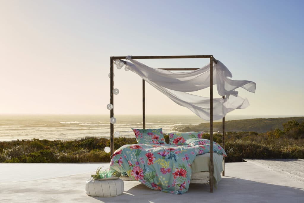 A bed standing on a sandy beach directly by the sea.