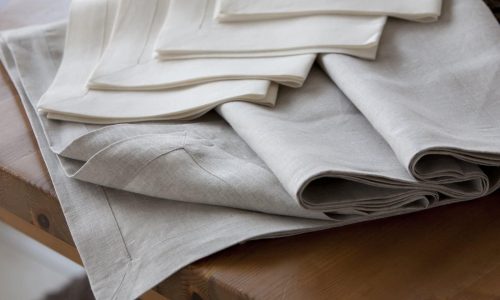 Ein Stapel ordentlich gefalteter beiger und cremefarbener Leinenservietten liegt auf einem Holztisch.