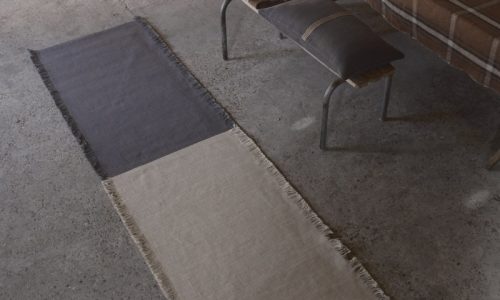 Eine Holzbank, die neben einem Teppich auf dem Boden steht.