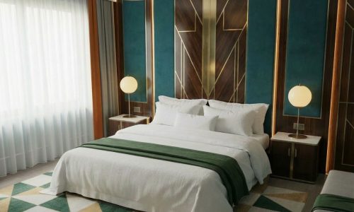 Ein modernes Schlafzimmer mit einem großen Bett in Frigg Halbleinen-Bettwäsche von Schlitzer Leinen, grünen Akzenten, runden Nachttischlampen und geometrischen Wandmustern in Teal, Holz und Gold unter den durchsichtigen Fenstern.