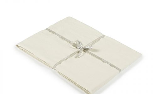 Das Heritage Oyster Bio Leinen Spannbettlaken von Libeco, ein cremefarbenes gefaltetes Bettlaken, das mit einem hellgrauen Band gebunden ist, wird auf weißem Hintergrund gezeigt.