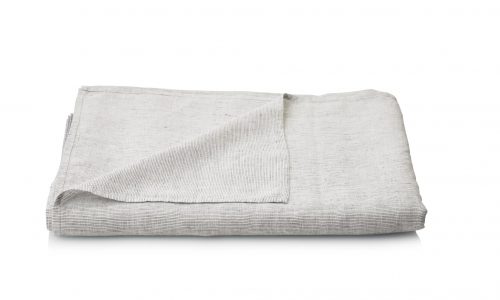A neatly folded light gray Junco linen bed sheet from Geniksa with a subtle textured pattern is shown on a white background with one corner turned up slightly to show the underside.
