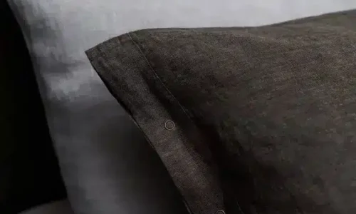 Close-up of two pillows – one in dark anthracite and one in light grey pillowcase – showing the texture of the fabric and the seams, styled with the Cygna Classic Linen Bedding by Geniksa.