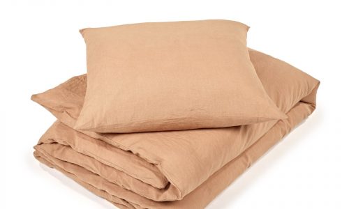 Ein hellbraunes Bettwäscheset, inspiriert von der Madison Cinnamon Farbige Leinen Bettwäsche von Libeco, besteht aus einer ordentlich gefalteten Bettdecke und einem passenden Kissen, alles auf einem weißen Hintergrund.