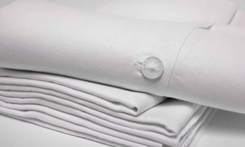 Abgebildet ist ein ordentlich gefalteter Stapel Starkes Leinen - Weiße Bettwäsche der Leinenweberei Hoffmann mit einer Nahaufnahme der geknöpften Manschette auf dem obersten Blatt vor einem schlichten weißen Hintergrund.