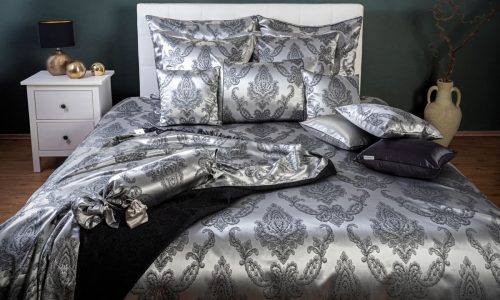 Ein Bett mit silberner und schwarzer Bettdecke und Kopfkissen.